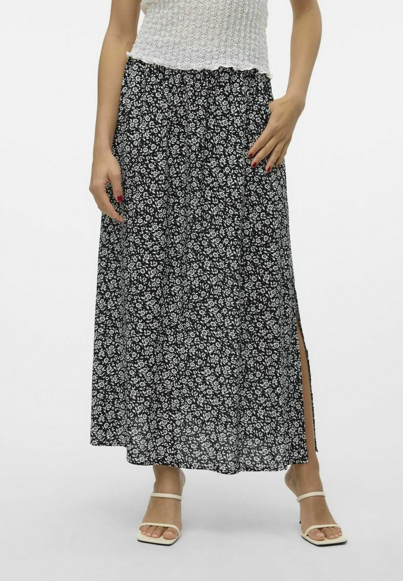 Femme portant une jupe midi florale noire et blanche avec une fente latérale, un top sans manches blanc texturé et des sandales blanches à lanières.