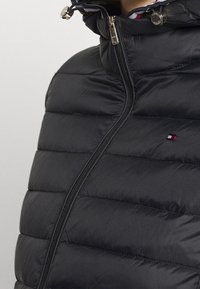 Zwarte gewatteerde jas met een hoge kraag, ritssluiting aan de voorkant en metalen accenten. Heeft een doorgestikte textuur en een klein, kleurrijk logo op de borst.