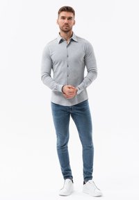 Grijze overhemd met lange mouwen, voorzien van een kraag en een effen textuur, gecombineerd met blauwe jeans en witte sneakers.