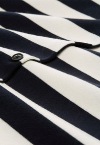 Marine- und weiß gestrefter Stoff mit weicher Textur. Verfügt über einen schwarzen Knopf und ein geschwungenes Kragen-Design, das ein geschichtetes Erscheinungsbild schafft.