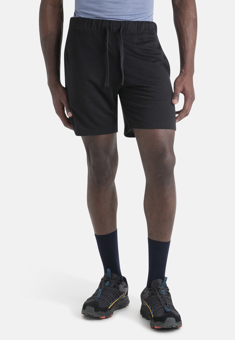 Pantalones cortos negros con cintura elástica y cordón, hechos de una tela suave. Combinados con zapatillas deportivas negras y calcetines azul marino.