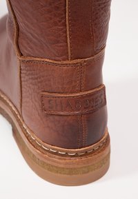 Brun läderkänga med strukturerad yta, som har en sydd sula och ett varumärkesmärke med texten "SHABBIES" på baksidan.