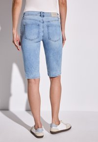 Ljusblå denimshorts med en åtsittande design, knälånga, med två bakfickor och en texturerad finish. Matchas med vita sneakers.