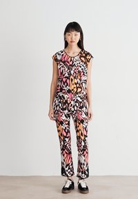 Fargerik mønstret jumpsuit med korte ermer. Har svarte, rosa, oransje og hvite abstrakte design. Slim fit, ankle-lengde bukser og flate sko.