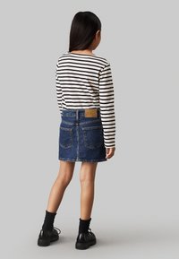 Camicetta a maniche lunghe a righe e gonna di jeans blu, con tasche posteriori e una patch con logo. Scarpe nere stringate con suole strutturate.