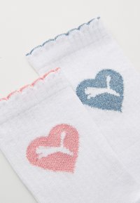 Weiße Socken mit gewelltem Bund, die mit pinken und blauen Herzmotiven sowie einem Silhouetten-Logo versehen sind. Weiches Material mit strukturiertem Stickerei.