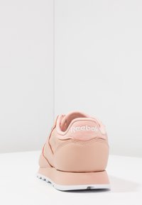 Ljusrosa Reebok-sneakers visade bakifrån på en vit yta med en vit vägg i bakgrunden.