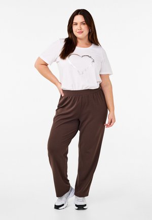 White t-shirt with metallic heart graphic and brown elastic-waist trousers. Model wears white and black athletic shoes. Smooth fabric texture.