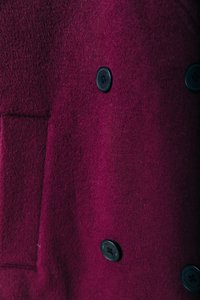 Casaco duplo em lã burgundy profundo com uma textura suave, apresentando dois botões pretos e um bolso lateral.