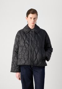 Zwarte gewatteerde jas met grote kraag, voorzien van een ruitpatroon, knopen aan de voorkant en zijzakken; gecombineerd met donkere denimjeans.