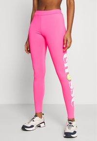 Różowe legginsy z elastycznego materiału mają wysoki pas, nadrukowany tekst na boku oraz akcent w postaci żółtej buźki.