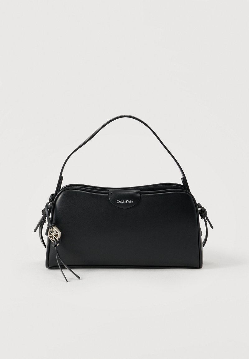 Μαύρη δερμάτινη τσάντα χειρός με δομημένο σχέδιο, που διαθέτει κοντή λαβή, κλείσιμο με φερμουάρ και μεταλλικό λογότυπο. Προσαρτημένο διακοσμητικό φούντα.