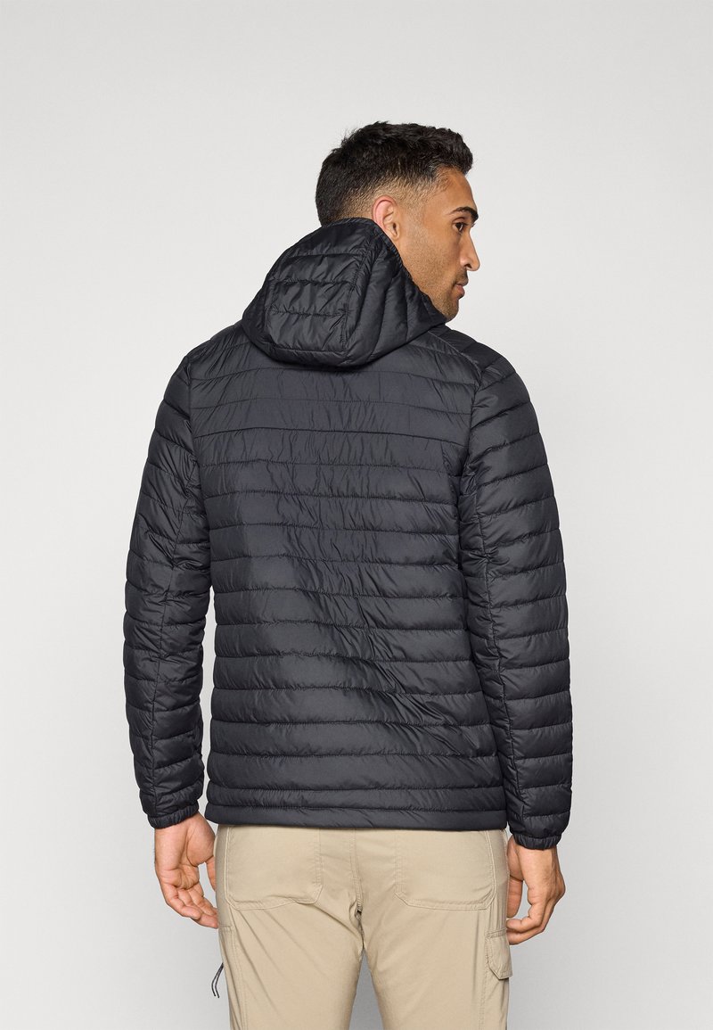 Chaqueta negra acolchada con capucha, con diseño acolchado, textura suave y puños elásticos. Vista desde la parte de atrás.