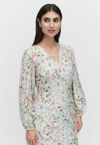 Kukallinen mekko kevyestä kankaasta, jossa on V-pääntie, pitkät puffihihat ja monivärisiä kukkakuoseja vaaleancreme-taustalla.