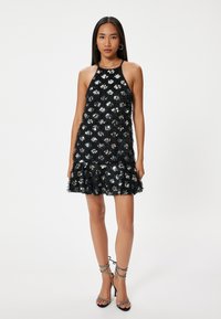 Robe noire à encolure halter avec un design à franges texturées, ornée de sequins irisés. Comprend un ourlet à volants et des bretelles fines.