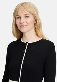 Cardigan noir avec une patte de boutonnage et des finitions blanches, doté d'un col rond et de manches longues, fabriqué en tissu tricoté texturé.