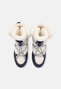 Hvide, bløde støvler med en marineblå gummibund. Har en tofarget snørebåndsløsning og en ombukkelig krave. Teksturerede stofdetaljer.