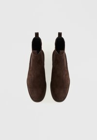 Bottines Chelsea en suède marron avec des panneaux élastiques sur les côtés, bout arrondi et languette à l'arrière. Texture lisse, design minimaliste, semelle plate.
