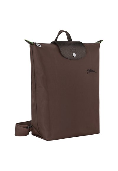 Brown nylon backpack with a textured leather flap and a green accent, featuring a zip closure and a flat strap. Logo embroidered on front.