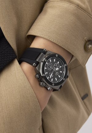 Črn časovnik z teksturirano črno gumijasto naravnos, šestkotno srebrno ohišje in črnim številčnico, ki vključuje srebrne poudarke in funkcije kronografa.