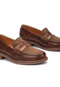 Mocasines de cuero marrón con detalles de ante en la parte superior, que presentan costuras de contraste y un tacón bajo apilado. Superficies suaves y texturizadas.