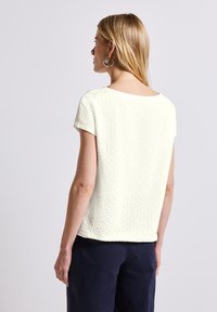 T-shirt med korte ærmer i struktureret, lysecrème stof med en afslappet pasform og bred halsudskæring, parret med mørke, løstsiddende bukser.