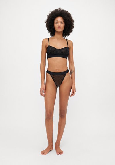 Zwart polka dot lingerie set gemaakt van transparante stof, met een bralette met verstelbare straps en bijpassende hooggehaakte slipjes.