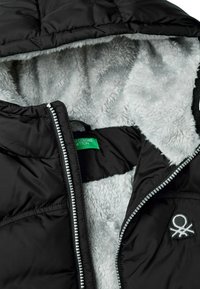 Giacca a vento nera con fodera grigia pelosa, zip argentata e piccolo design ricamato. Presenta un cappuccio e un'etichetta interna nascosta.