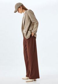 Brown checkered blazer, cream top, brown wide-leg pants, and beige block-heeled shoes, paired with a matching cap.
