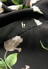 Zwart bloemig stof met lichtgekleurde magnolia patronen. Inclusief een gouden accent met de letter "b." Glad textuur en gedetailleerde stiksels.