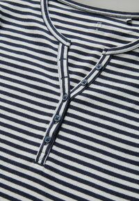 Marineblå og hvid stribet henley skjorte med knaplukning, ribbet tekstur og kontrasterende krave. Fire blå knapper synlige.