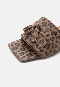 Καφέ σαουέτ μύλος με σκούρο λεοπάρ μοτίβο, τετράγωνη μύτη, φαρδιά λουρίδα και διπλές λεπτομέρειες με φουντίτσες στην κορυφή.