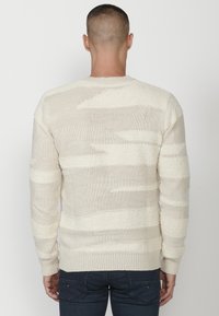 Pletený sveter v off-white farbe s textúrovanými pruhmi, s okrúhlym výstrihom a rebrovanými manžetami. Voľný strih so zmesou hladkých a nadýchaných textúr.
