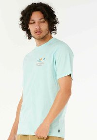 Mintgrünes T-Shirt mit kurzen Ärmeln aus weichem Baumwollstoff, ausgestattet mit einem grafischen Druck von Sonne und Palmen auf der Brust, Rundhalsausschnitt und seitlichem Etikett.