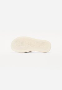 Semelle de chaussure en matériau beige texturé avec "BOGENER" en lettres majuscules embossé au centre. Les bords arrondis améliorent l'adhérence.
