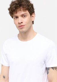 Tricou alb din bumbac, cu guler rotund, mâneci scurte și un detaliu discret al logo-ului pe partea stângă a pieptului, textură fină și croială normală.