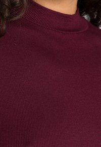 Maglione a collo alto a coste bordeaux realizzato in un materiale elastico; presenta un colletto alto e una superficie liscia.