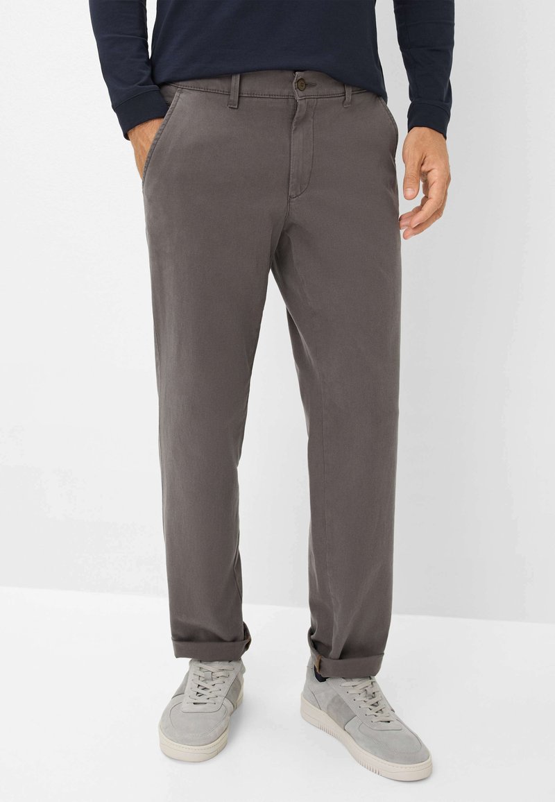 Grijze katoenen chinos met zijzakken, een verticale knoopsluiting en opgerolde mouwen. G gedragen met lichtgrijze sneakers.