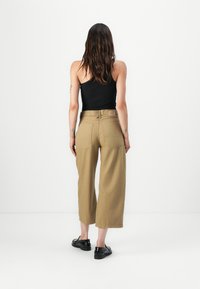 Pantaloni khaki larghi con vita alta, texture del tessuto visibile, due tasche posteriori, abbinati a scarpe slip-on nere.
