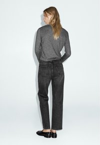 Una maglietta grigia a maniche lunghe abbinata a jeans in denim neri a vita alta, con tasche posteriori e un taglio dritto, completata da scarpe nere.
