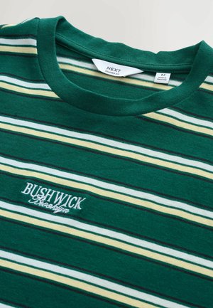 Green striped t-shirt made from soft fabric. Features white, yellow, and dark green stripes with "BUSHWICK" text embroidered in white.