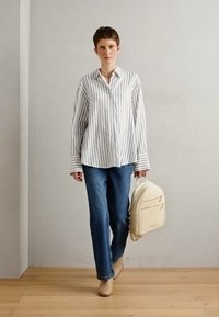 Stripet knapp-up skjorte i hvit og marineblå, blå jeans, beige ryggsekk med to glidelåslommer, og lyse beige sko. Minimalistisk design.