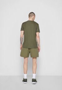 Oliwkowy t-shirt sportowy z krótkimi rękawami, w połączeniu z pasującymi szortami. Teksturowana tkanina, prosty krój oraz białe skarpetki z zielonymi butami.