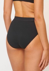 Hochtaillierte schwarze Baumwollunterwäsche mit glatter Textur, die einen Spitzenrand entlang der Beinausschnitte und ein nahtloses Rückendesign aufweist.