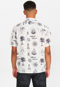Košile s krátkým rukávem vyrobená z bílého materiálu se černými námořními vzory, včetně lodí, palm a kompasů.