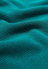 Getextureerde teal stof met een ribbelpatroon. Het materiaal lijkt zacht en iets rekbaar, met een mooie weergave van golven en plooien.