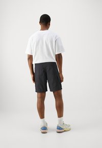 Svarta cargoshorts med sidfickor, ihop med en vit t-shirt med kort ärm, bärs med grå sneakers och vita strumpor.