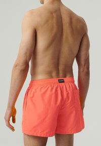 Jasnoróżowe kąpielówki z elastycznym pasem, bocznymi kieszeniami oraz małą kieszenią z tyłu. Gładka tekstura i nowoczesny krój.