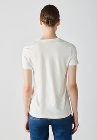 Cream-colored short-sleeve t-shirt with a crew neck, soft texture, and slightly tapered fit. Features a plain design, no visible patterns or accents.