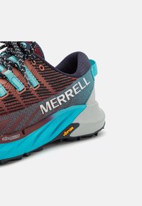 Gros plan d'une chaussure de trail Merrell bleu et marron avec des lacets noirs, une semelle Vibram et un col rembourré à la cheville sur fond blanc.